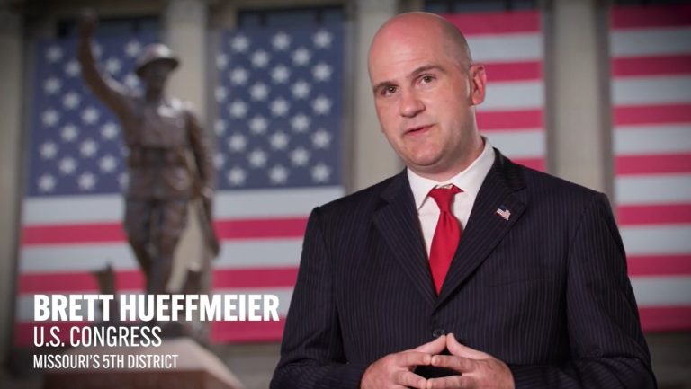 Brett Hueffmeier in foreground, courthouse with American Flag banners in background